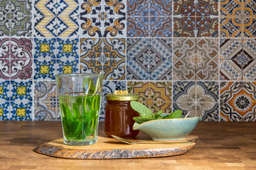 Wooden cuttingboard with fresh mint tea in a glass mint herbs in bowl a golden spoon and a jar of...