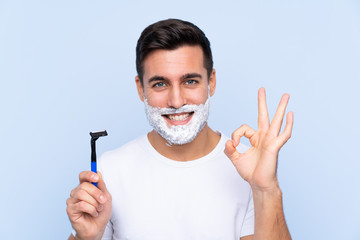 Young handsome man shaving his beard over isolated background showing ok sign with fingers