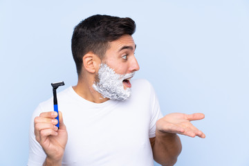 Young handsome man shaving his beard over isolated background with surprise facial expression