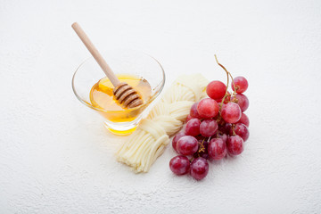 Pigtail cheese is decorated with a bunch of grapes, honey in a vase, on a white background. Cheese concept.