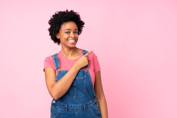African american woman with overalls over isolated pink background pointing finger to the side