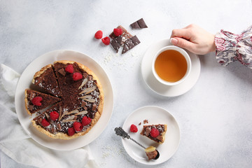 Chocolate cake with cottage cheese and raspberries. A cup of tea with hands on a light background. Background image, copy space