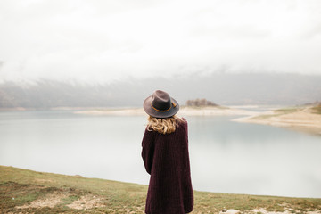 Happy beautiful woman in purple sweater holding her hat and enjoying trip on the lake. Female...
