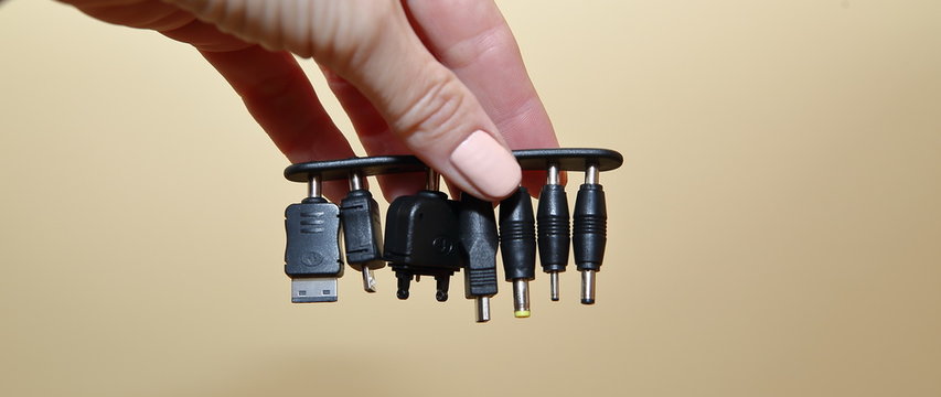 Few different ends used in chargers of electronic devices like smrt phones, tablets, computers, phones etc. in woman hand close up isolated on warm pastel color background
