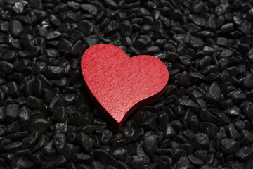 Red wooden heart on a black pebble background.