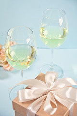 Two glasses with white grape wine with roses and gift box on the background. Romantic dinner concept.