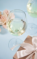 Two glasses with white grape wine with roses and gift box on the background. Romantic dinner concept.