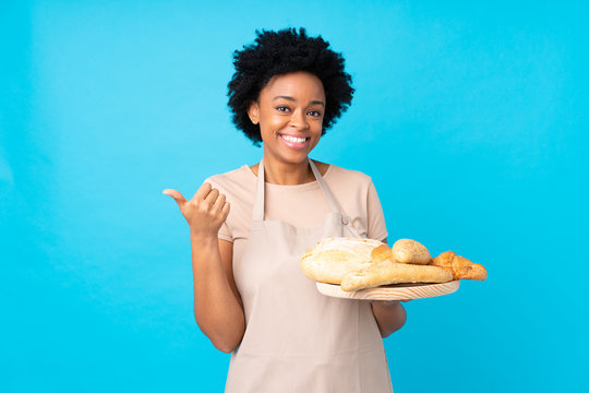 African american woman in chef uniform. Female baker holding a table with several breads pointing to the side to present a product