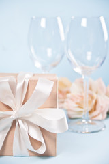 Fototapeta na wymiar Gift box with empty two wineglasses and flowers on the background. Romantic dinner concept.