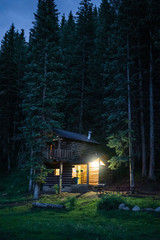 Cabin in woods at night with front porch light on