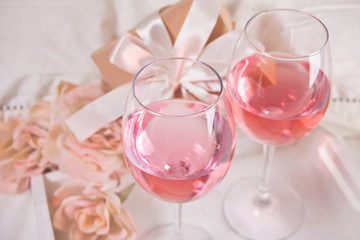 Two glasses with pink grape wine with flowers and gift box on the background. Romantic dinner concept.