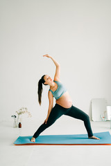a young pretty pregnant girl in sports clothes is doing yoga, doing asana on the Mat in the Studio