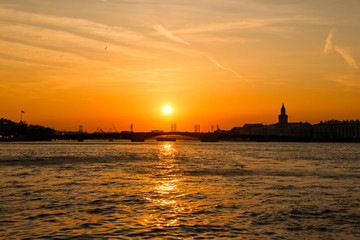 Cityscape of Saint Petersbrug city in Russia during sunset. View of the setting sun over the Neva River and the silhouettes of buildings and a bridge. Theme of travel in Russia.