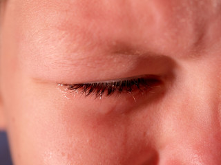 Naklejka premium Face of crying boy close up. Eyes, eyelashes, eyebrows, lips, teeth and tears. Emotions and grimaces of upset child