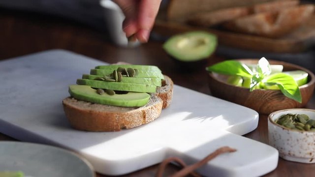 Hand sprinkles pepitas on an avocado toast. Healthy eating concept