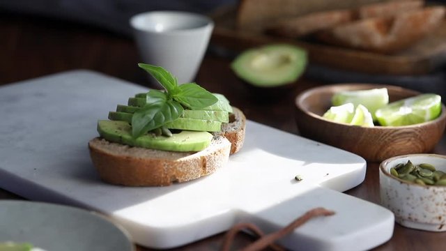 Hands decorate an avocado toast with fresh basil. Healthy eating concept