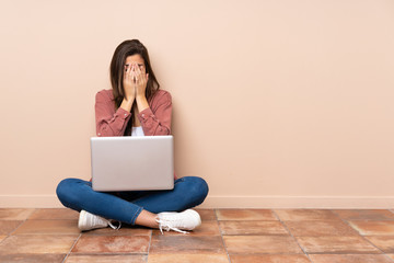 Teenager student girl sitting on the floor with a laptop with tired and sick expression