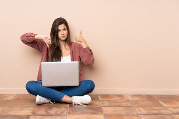 Teenager student girl sitting on the floor with a laptop making good-bad sign. Undecided between yes or not