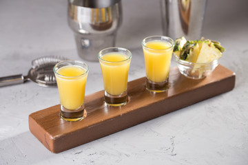 set of alcoholic cocktails in shot glasses with pineapple slices on wooden board