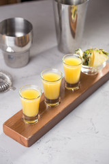 set of alcoholic cocktails in shot glasses with pineapple slices on wooden board