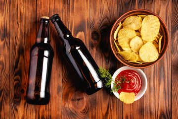 Two glass bottles of beer without a label with a snack in the form of potato chips with red sauce....