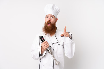 Redhead man using hand blender over isolated white background with surprise facial expression