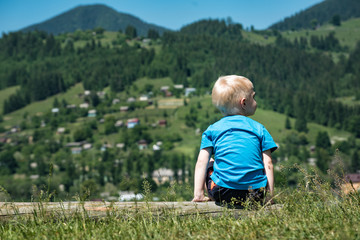 Fair-haired boy sits on nature background. Travel with little children. Back view