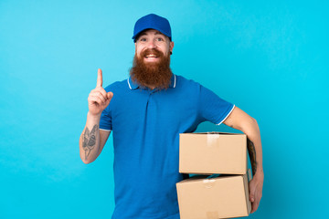 Redhead delivery man over isolated blue background pointing up a great idea
