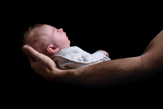 Baby in the arms of his father. Birth concept. Black background side view. Isolated