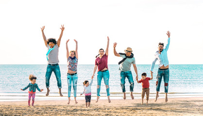 Happy multiracial families jumping together at beach holding hands - Summer vacation concept with...