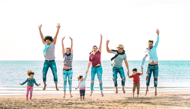 Happy multiracial families jumping together at beach holding hands - Summer vacation concept with young mixed race people having genuine fun outdoors enjoying sunset - Vivid azure backlight filter