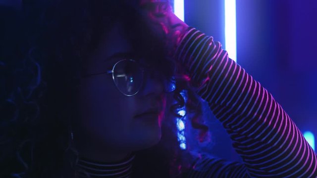 Neon girl portrait. Disco lounge. Thoughtful young woman playing with curly hair in blue pink glow.