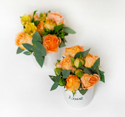 flower arrangement of orange roses and green leaves of eucalyptus in a vintage pot on a white...