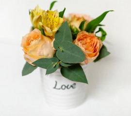 flower arrangement of orange roses and green leaves of eucalyptus in a vintage pot on a white...