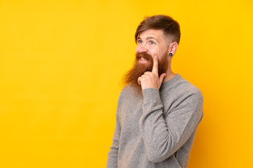 Redhead man with long beard over isolated yellow background thinking an idea while looking up