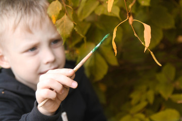 The boy paints the leaves in autumn green.