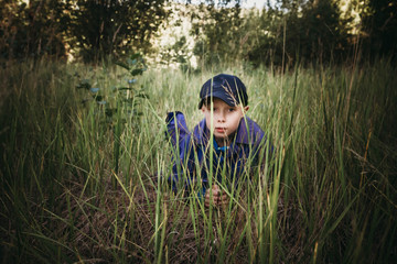 The boy is hiding in the grass. A boy plays in spies.