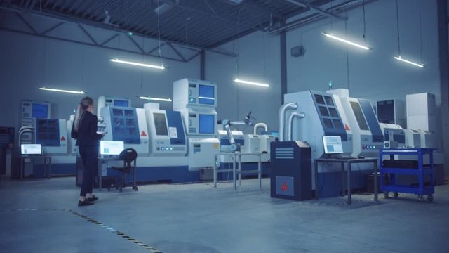 Industry 4.0 Modern Manufacturing Factory Lights Turning On: Female Chief Engineer And Operator Enters Fully Automated Workshop With Contemporary CNC Machinery And Assembly Line Robot Arm