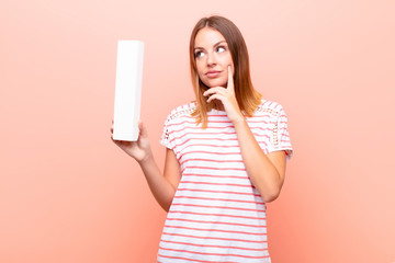 young pretty red head woman confused, doubtful, thinking, holding the letter I of the alphabet to...