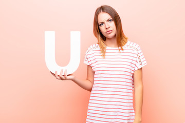 young pretty red head woman angry, anger, disagreement, holding the letter U of the alphabet to...