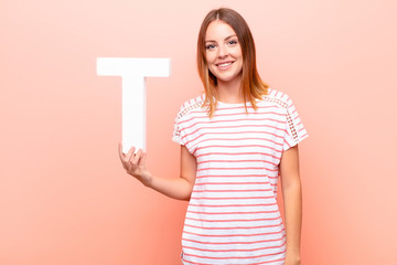 young pretty red head woman excited, happy, joyful, holding the letter T of the alphabet to form a...