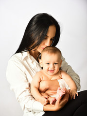 Newborn baby in a tender embrace of mother. Woman is playing with her baby. Mother playing with her baby. Family portrait of mum and child. Mother and baby kissing and hugging.