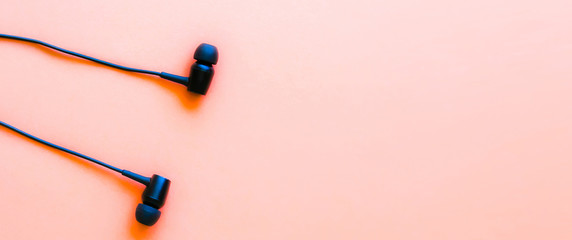 Earphones lying on the pink background. Modern music concept. Audio technology.