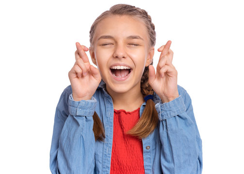 Portrait of teen girl crossing her fingers and wishing for good luck, isolated on white background. Caucasian teenager praying with crossed fingers and eyes closed. Child face expression emotions.