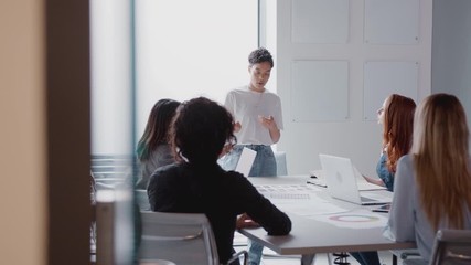 View Through Door As Female Boss Gives Presentation To Team Of Businesswomen Meeting Around Table 
