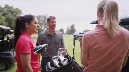 Group Of Male And Female Golfers Standing By Golf Buggy On Course And Choosing Clubs