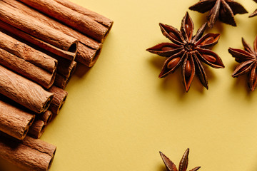 Close-up of spices: cinnamon sticks and star anise on a yellow background shot from above.