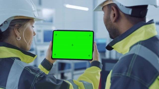 Industry 4.0 Factory: Chief Engineer and Project Supervisor in Safety Vests and Hard Hats, Talk, Use Digital Tablet Computer with Green Screen, Chroma Key. Workshop with Machinery. Zoom Out