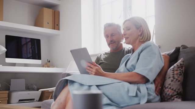 Senior Couple Sitting On Sofa At Home Using Digital Tablet Together
