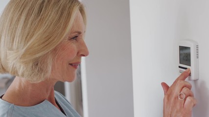 Close Up Of Mature Woman Adjusting Central Heating Temperature At Home On Thermostat